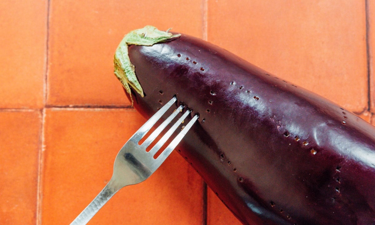 A fork pricking the skin of an eggplant.