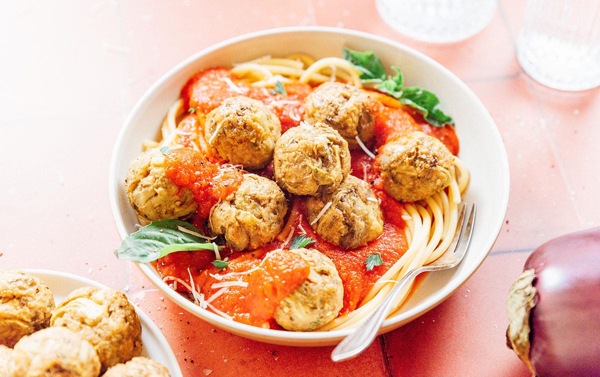 A white bowl of spaghetti topped with sauce and vegetarian meatballs.