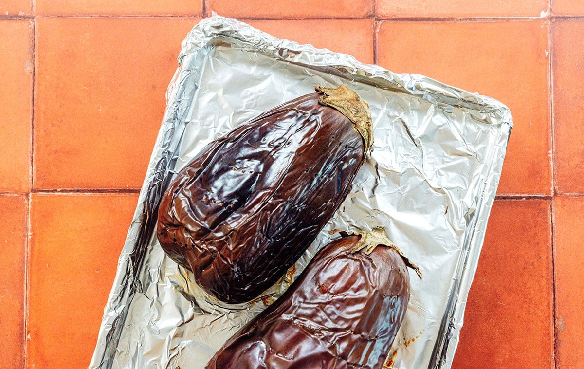 Two roasted eggplant on a foil lined baking sheet.