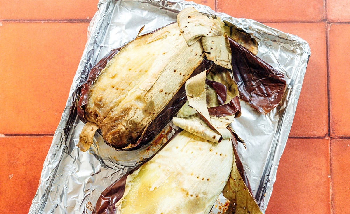 Peeling the skin off roasted eggplant on a foil lined baking sheet.