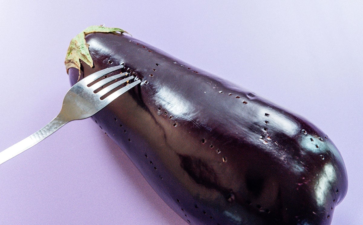 A fork pricking holes in an eggplant.