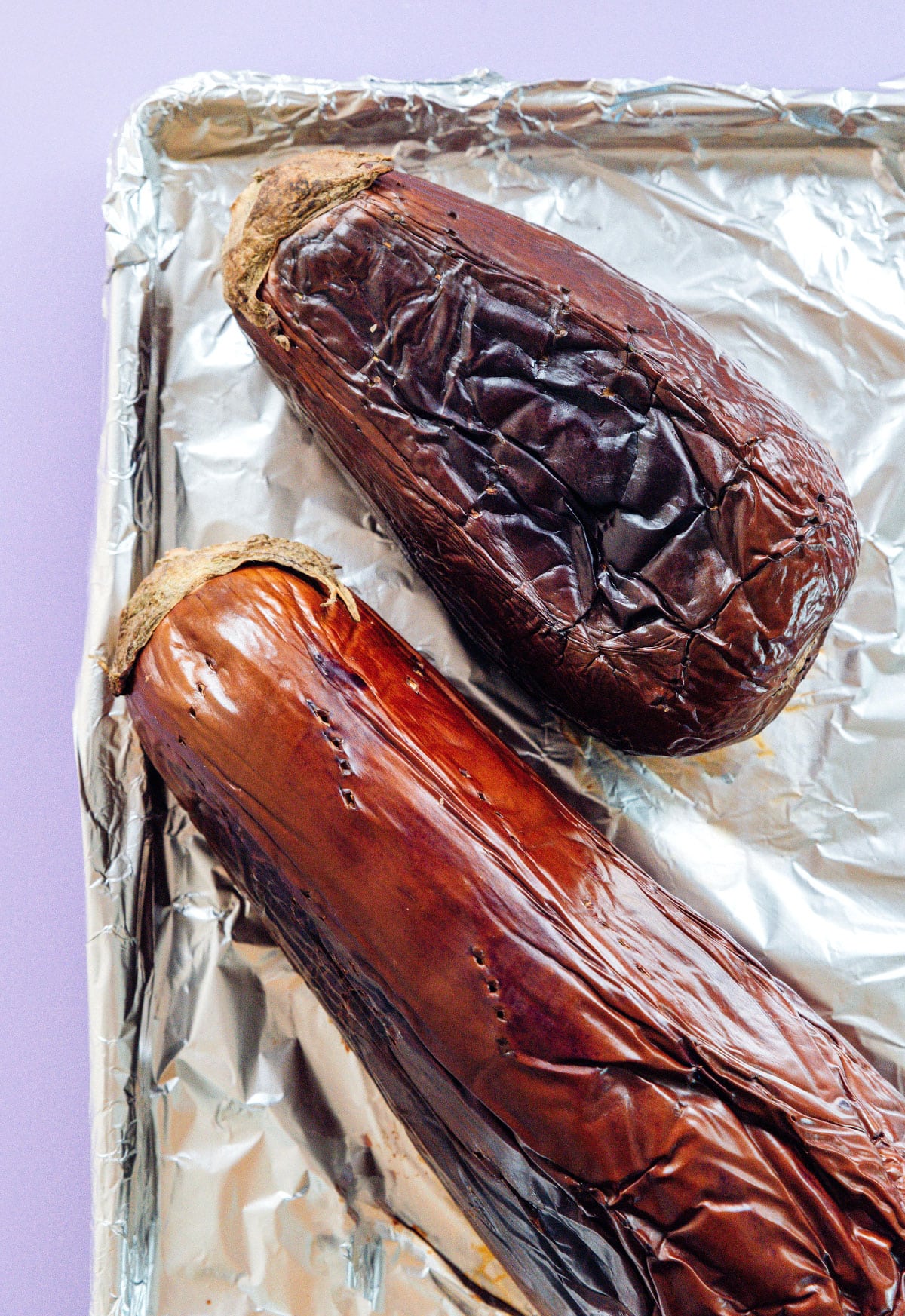 Roasted eggplants on a foil lined baking sheet.