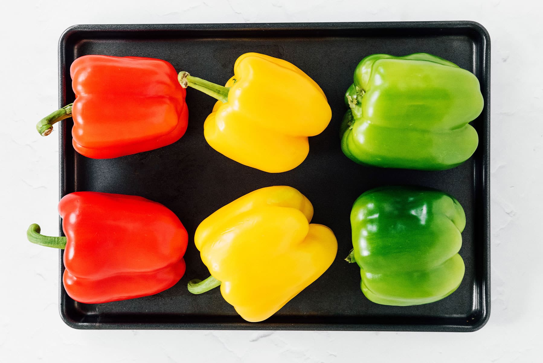 Red, yellow, and green bell peppers on a black tray.