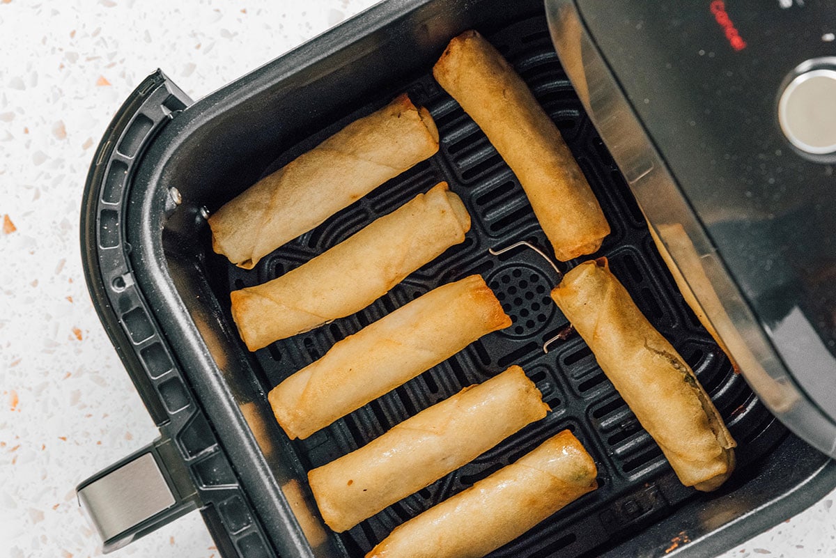 Spring rolls arranged in an air fryer basket with space between.