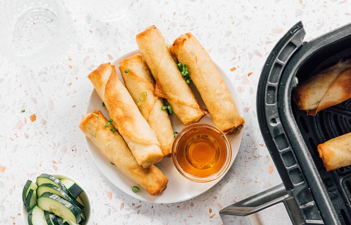 Fried spring rolls on a plate next to an air fryer basket.
