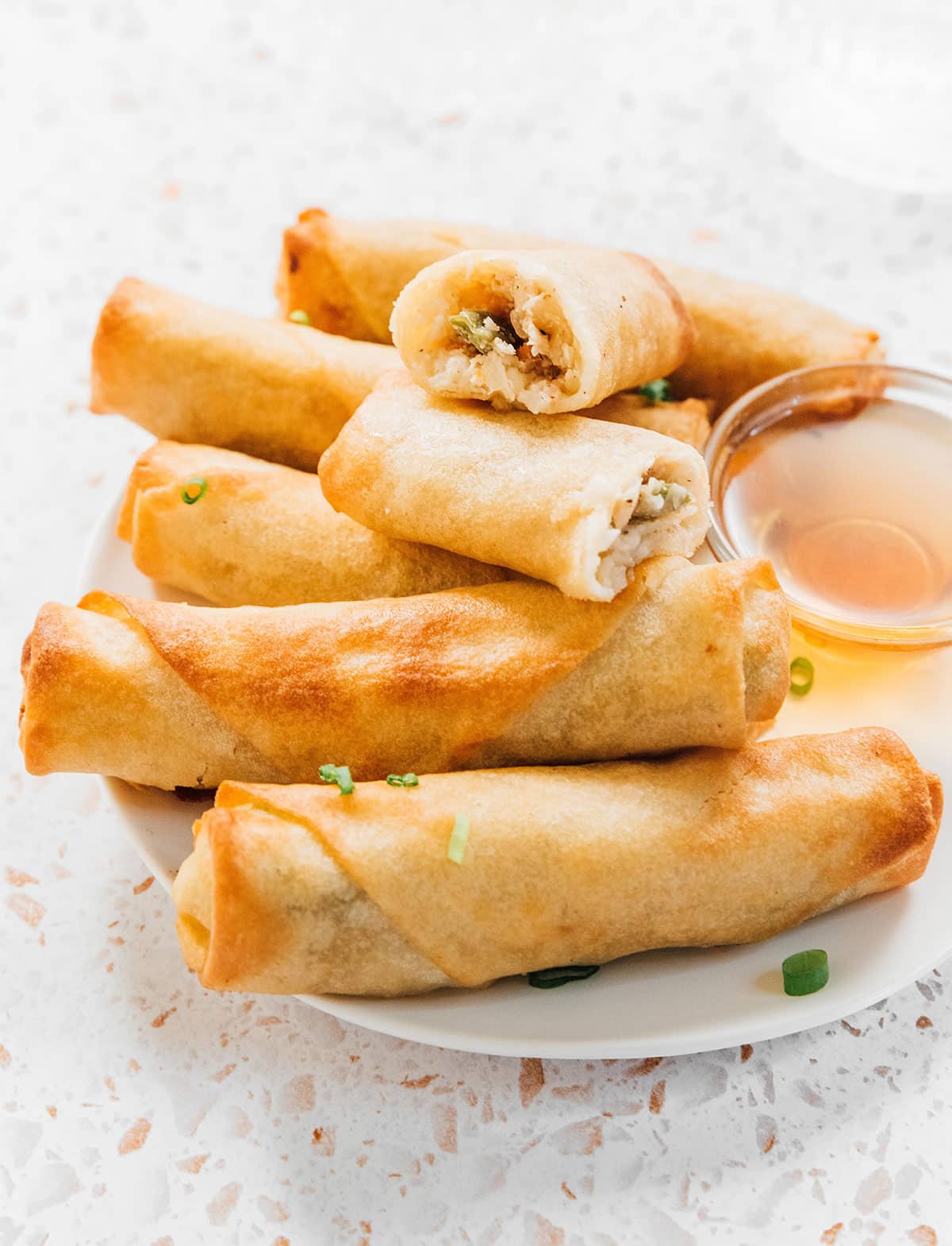 Air fried frozen spring rolls on a plate with one cut open to show the perfectly cooked inside and golden exterior.