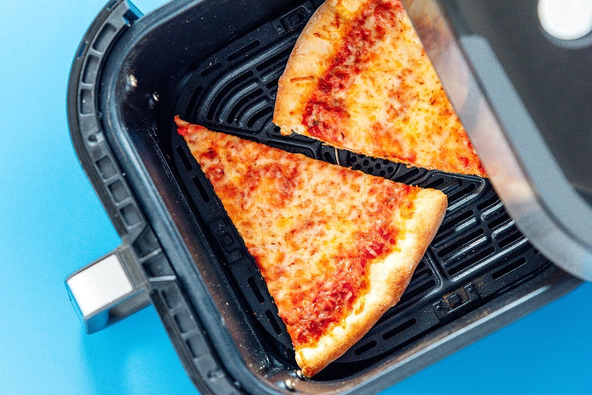Two slices of cheese pizza in an air fryer basket.