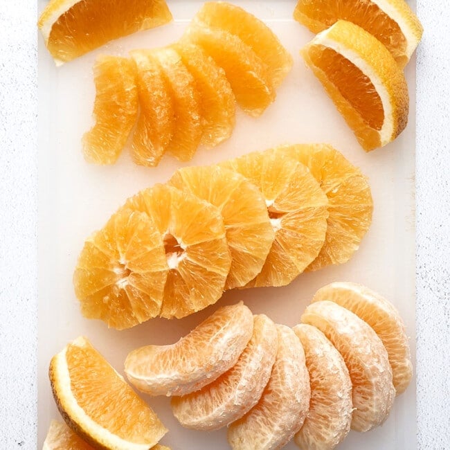 Many ways to cut an orange on a white cutting board.