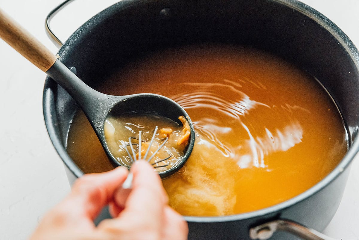 A ladle being dipped into the broth with the miso being whisked in the broth and the ladle.