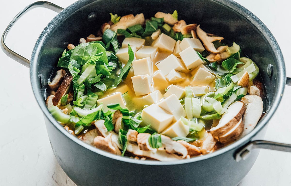 A pot with miso broth, tofu, bok choy, and mushrooms in it.