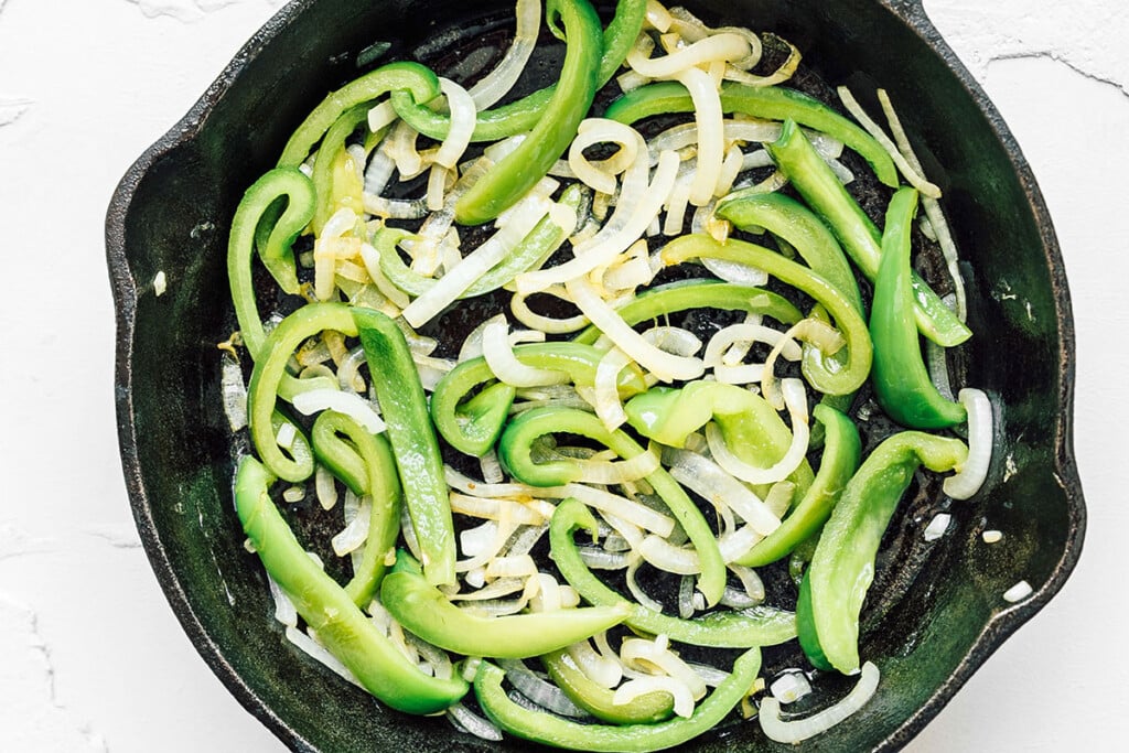 Green bell peppers and onions in a cast iron pan.