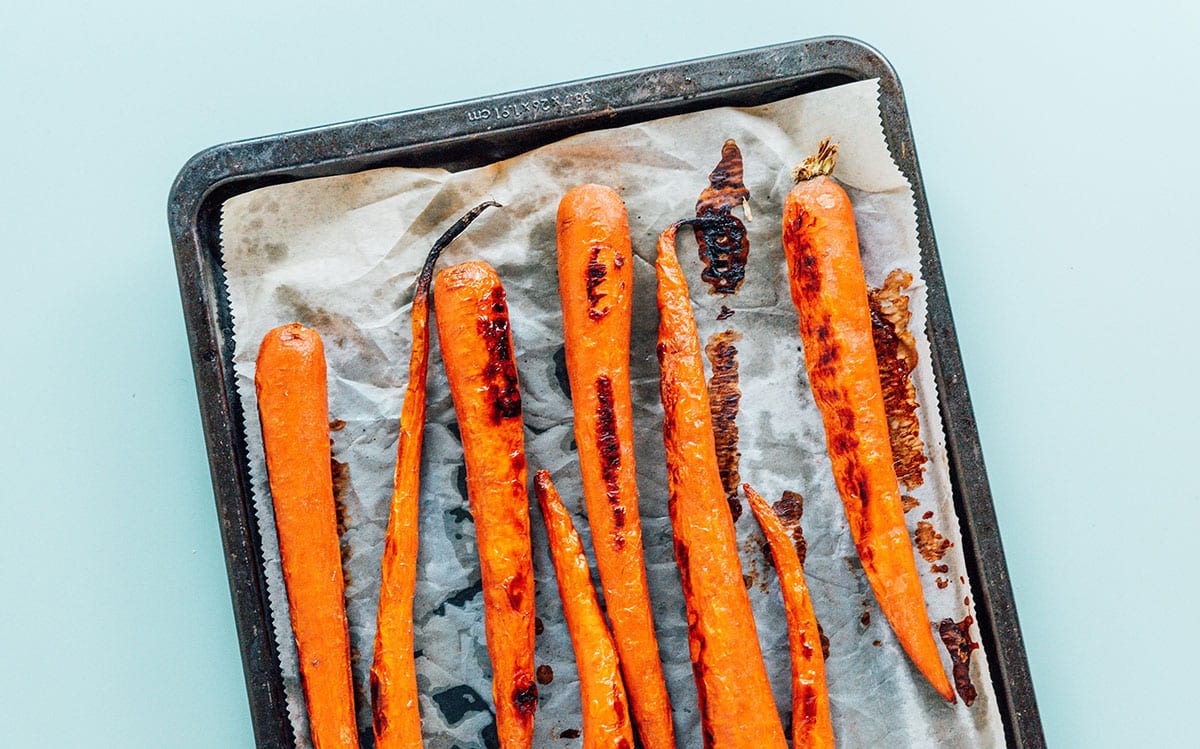 Roasted whole carrots on parchment paper on top of a baking sheet.