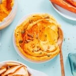 Carrot hummus on a plate with a wooden spoon.