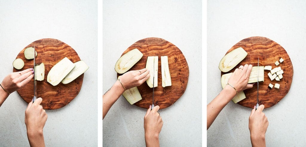 Slicing eggplant into cubes on a wooden cutting board.