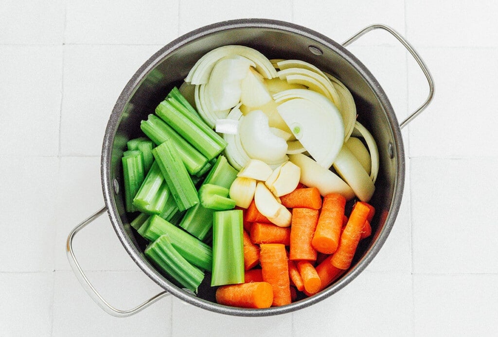 Chopped celery, carrots, peeled onions, and peeled garlic in a large pot before liquid is added. 
