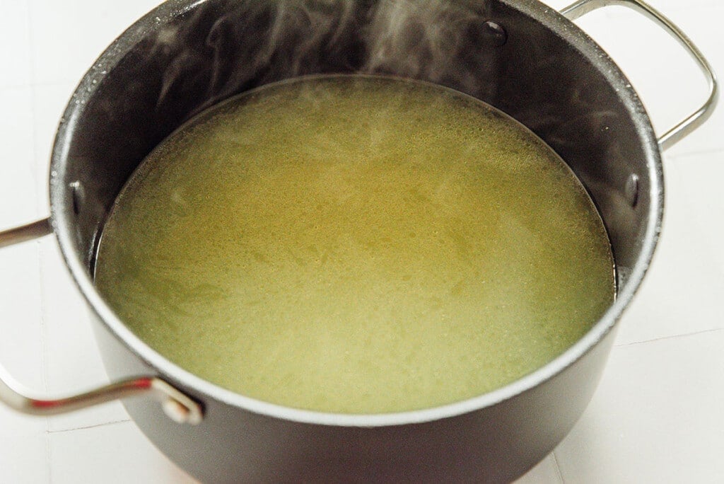 Broth from fresh vegetables steaming in a black pot. Set on a white background.