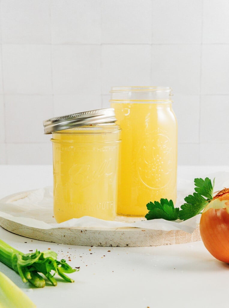 Yellow broth in class jars with metal lids. White background.