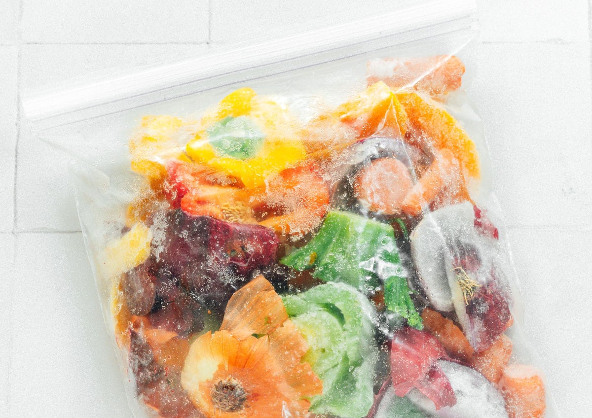Frozen vegetable scraps in a plastic bag on a white background.