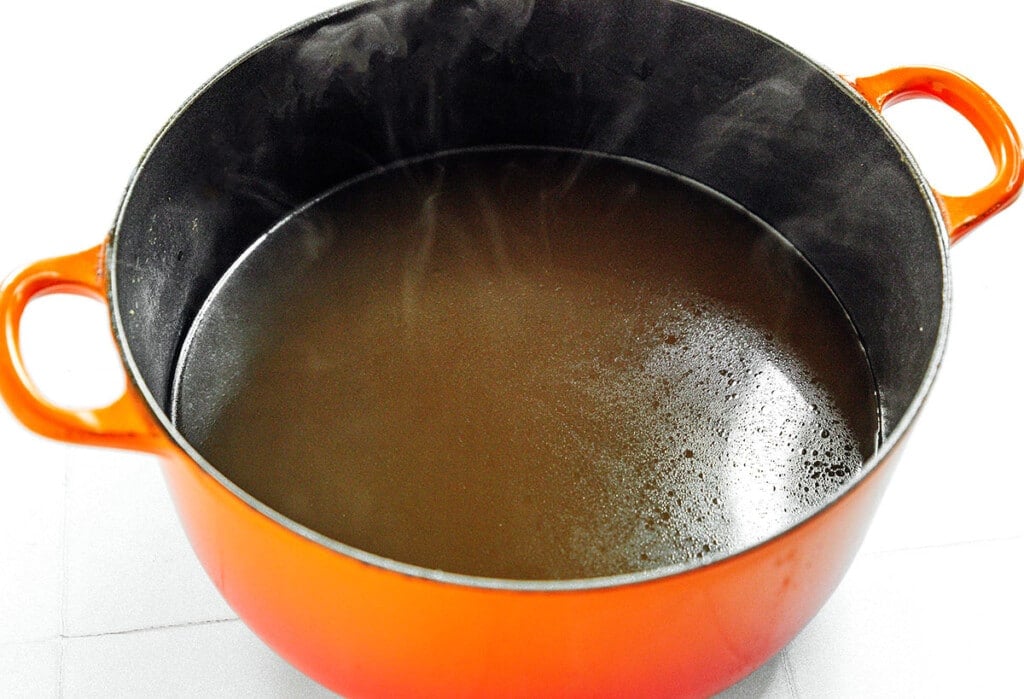 Broth from vegetable scraps steaming in an orange pot