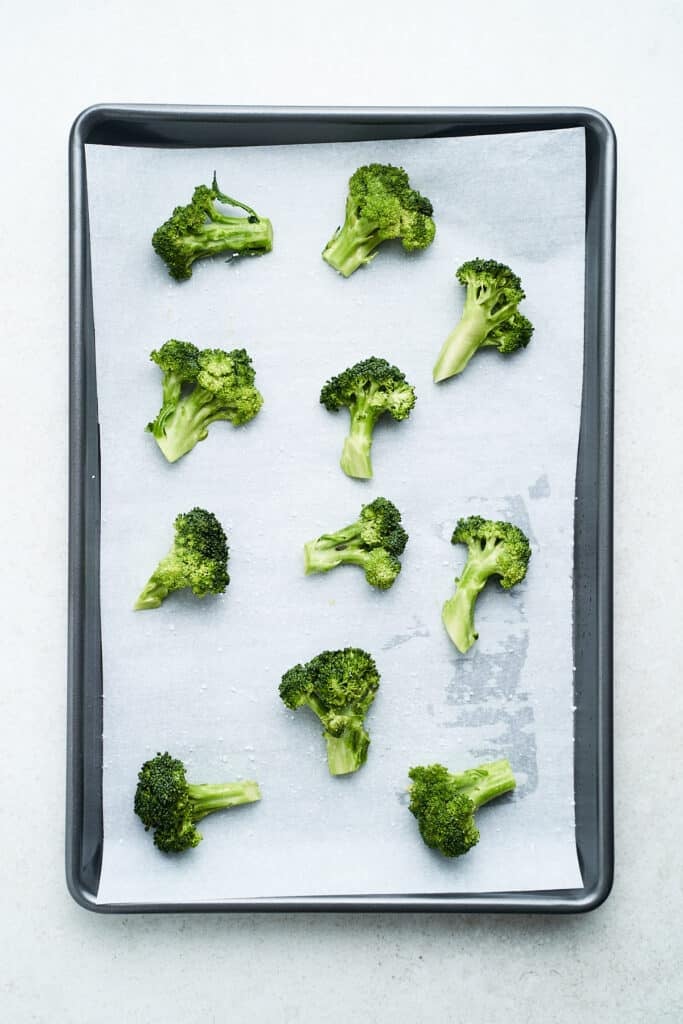 Raw broccoli on a lined baking pan.