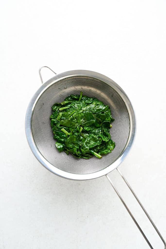 Blanched spinach in a strainer.