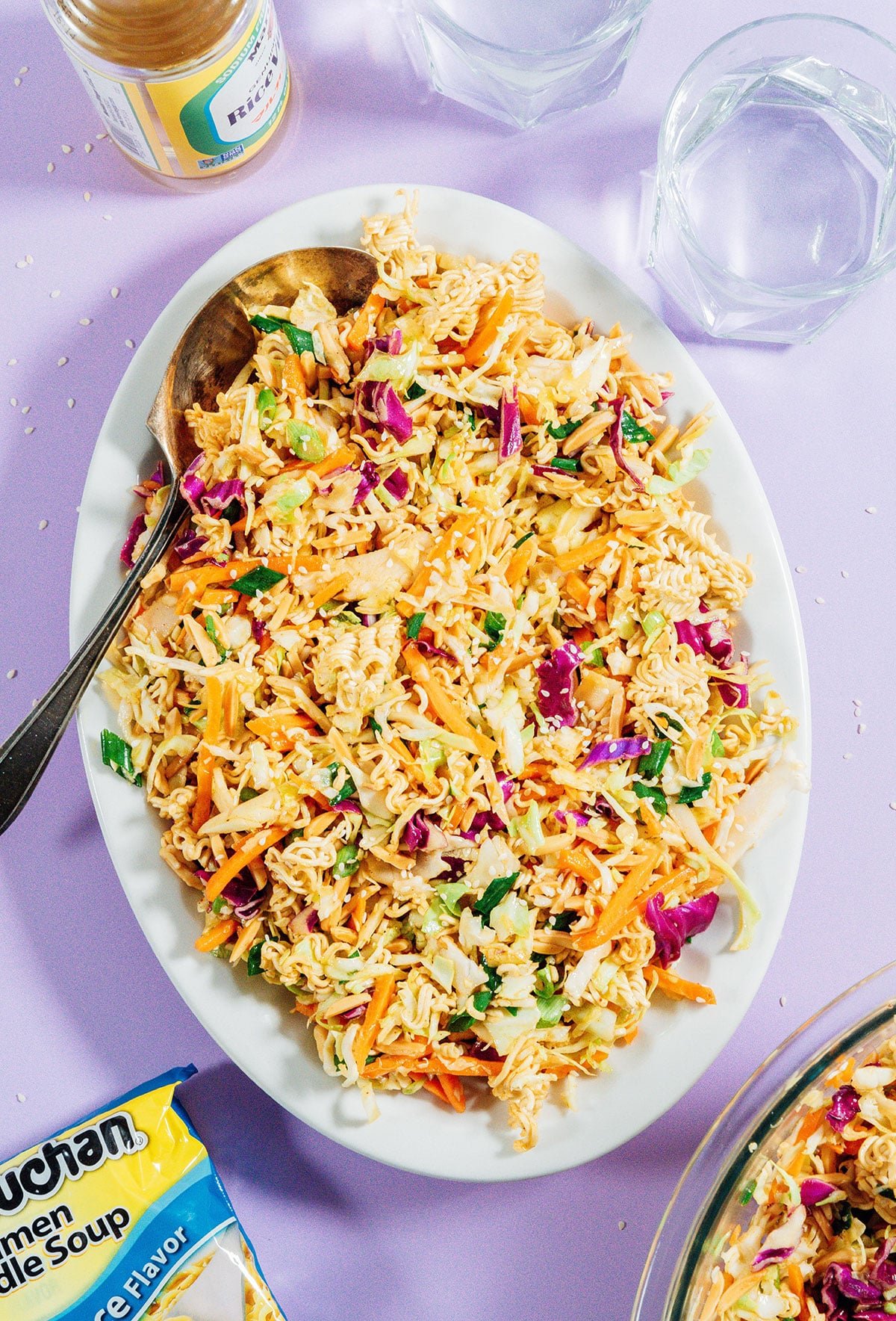 Ramen salad on a platter with a serving spoon on a purple background.