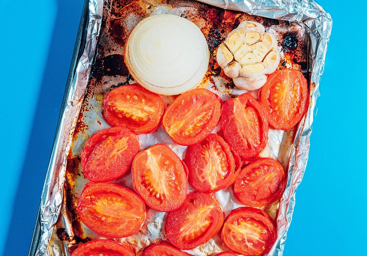 Roasted tomatoes, onion, and garlic on a sheet pan.