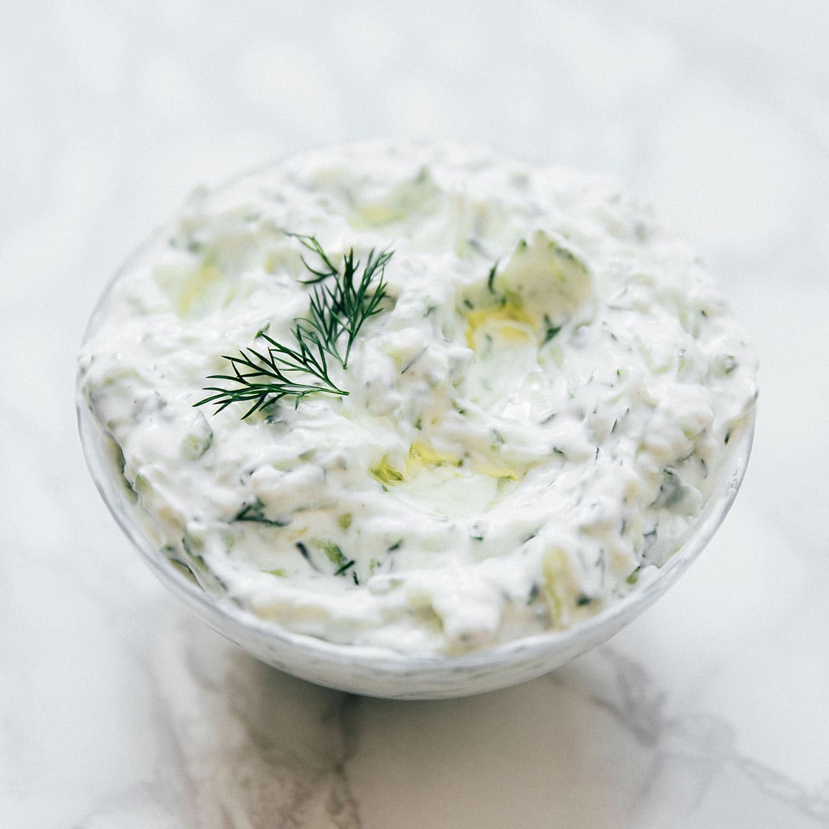 Tzatziki in a glass bowl on marble background.