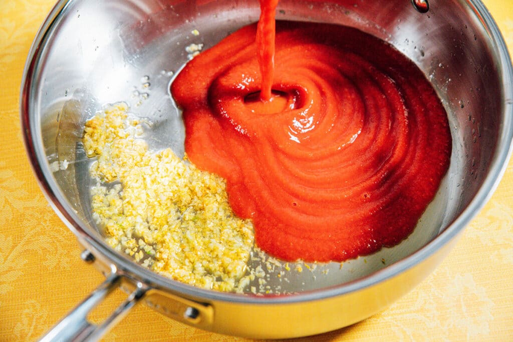 Adding tomato sauce to a pan with garlic.