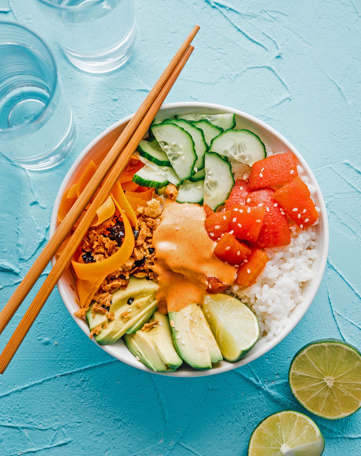 Vegan tomato tuna sushi bowl with rice, avocado, and cucumber in a bowl on a blue background
