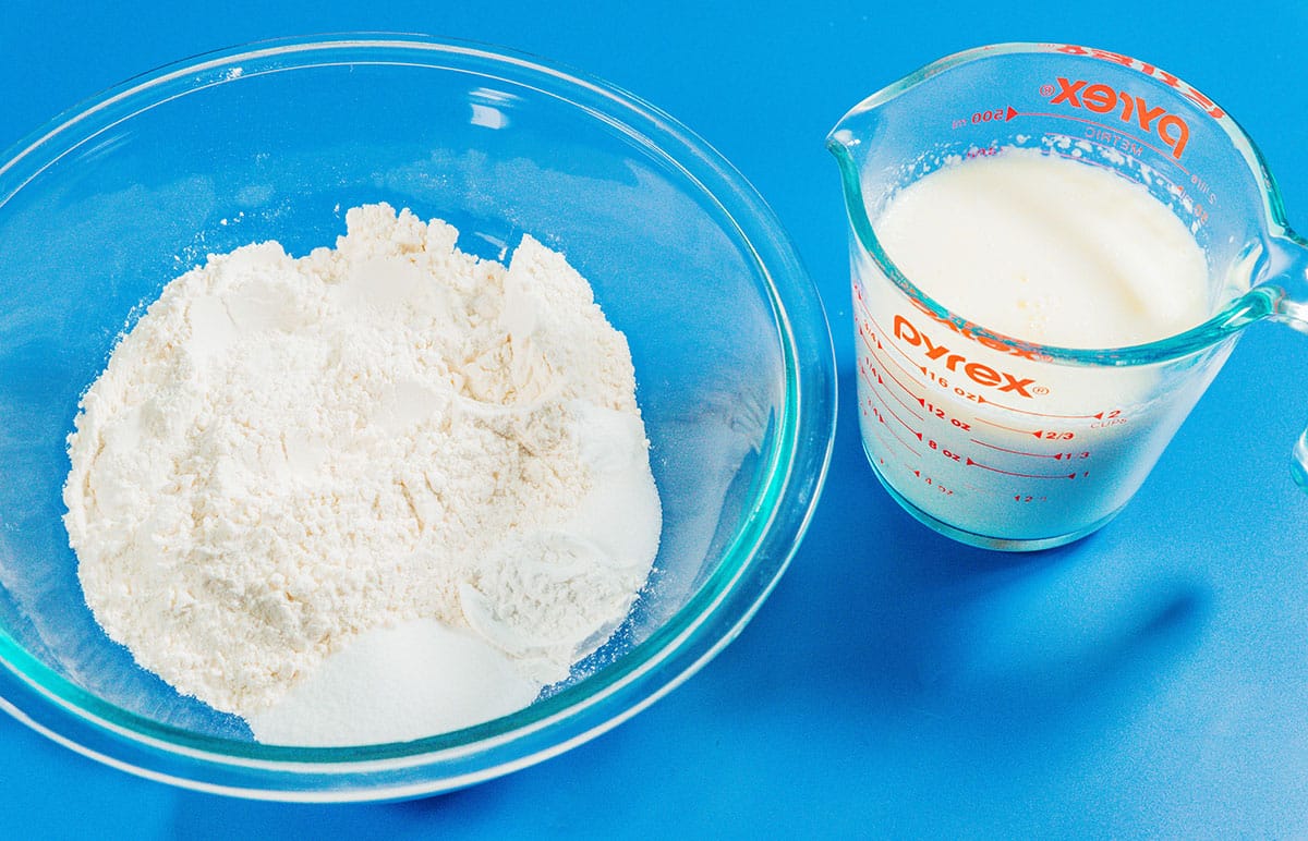 Flour in a glass bowl next to a pyrex glass of milk.