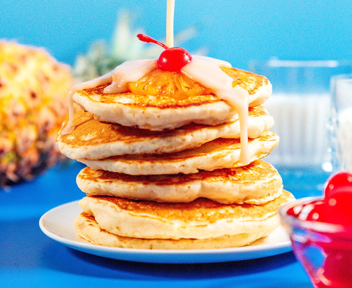Pineapple upside down pancakes stacked with a cherry on top.