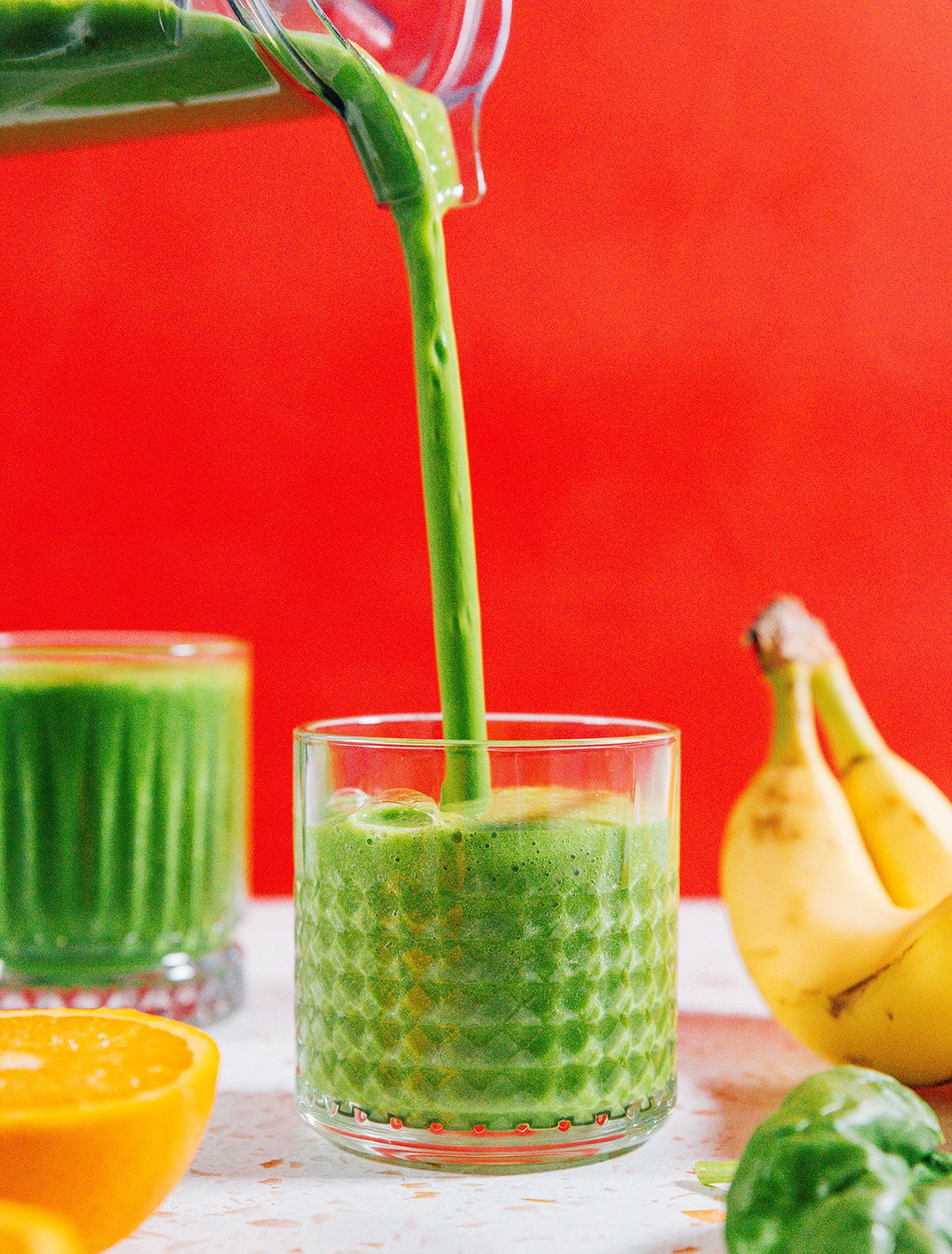 Green smoothie in a glass with red background.