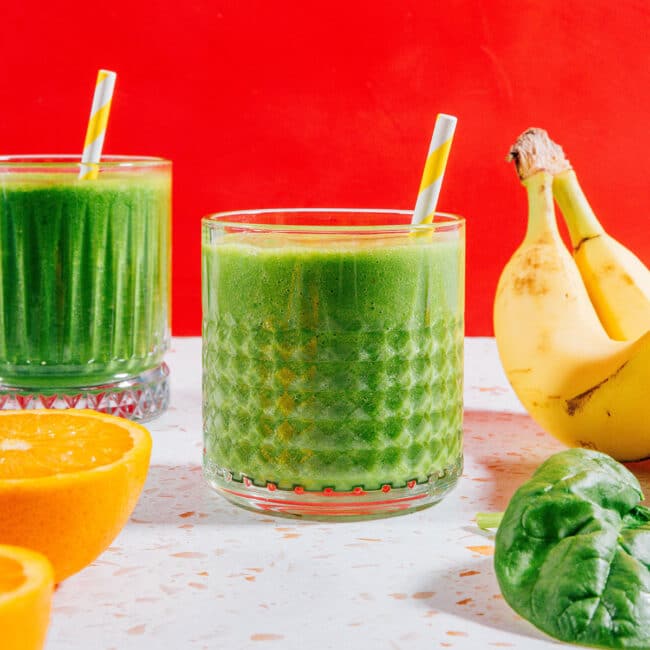 Green smoothie in a glass with red background.