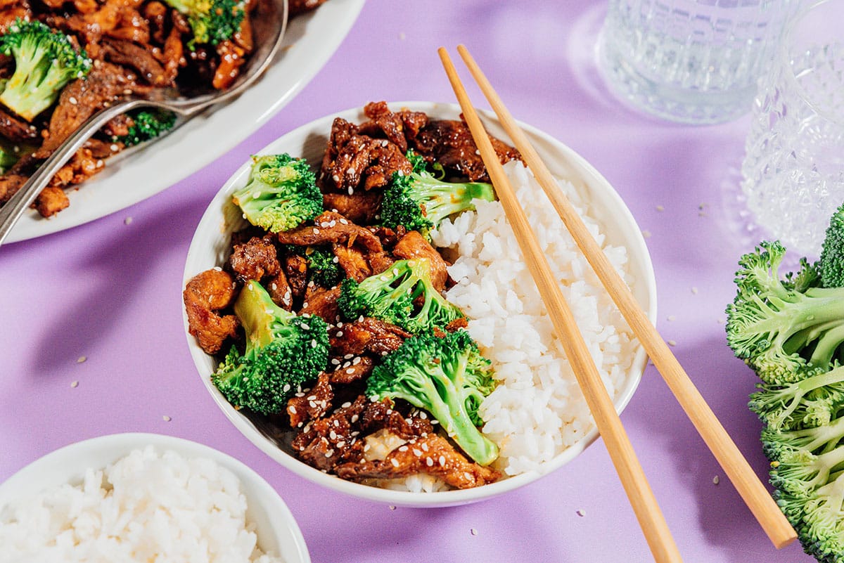 Vegan beef and broccoli with rice on a purple table.