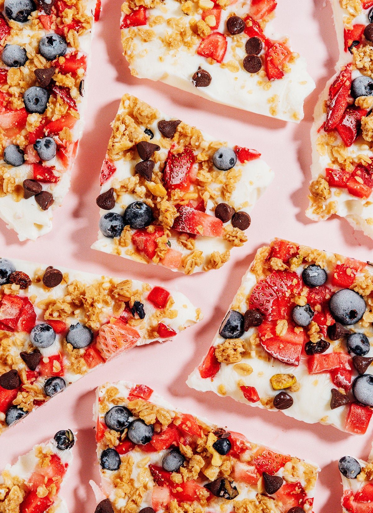 Frozen yogurt breakfast bark with berries and granola on a pink background.