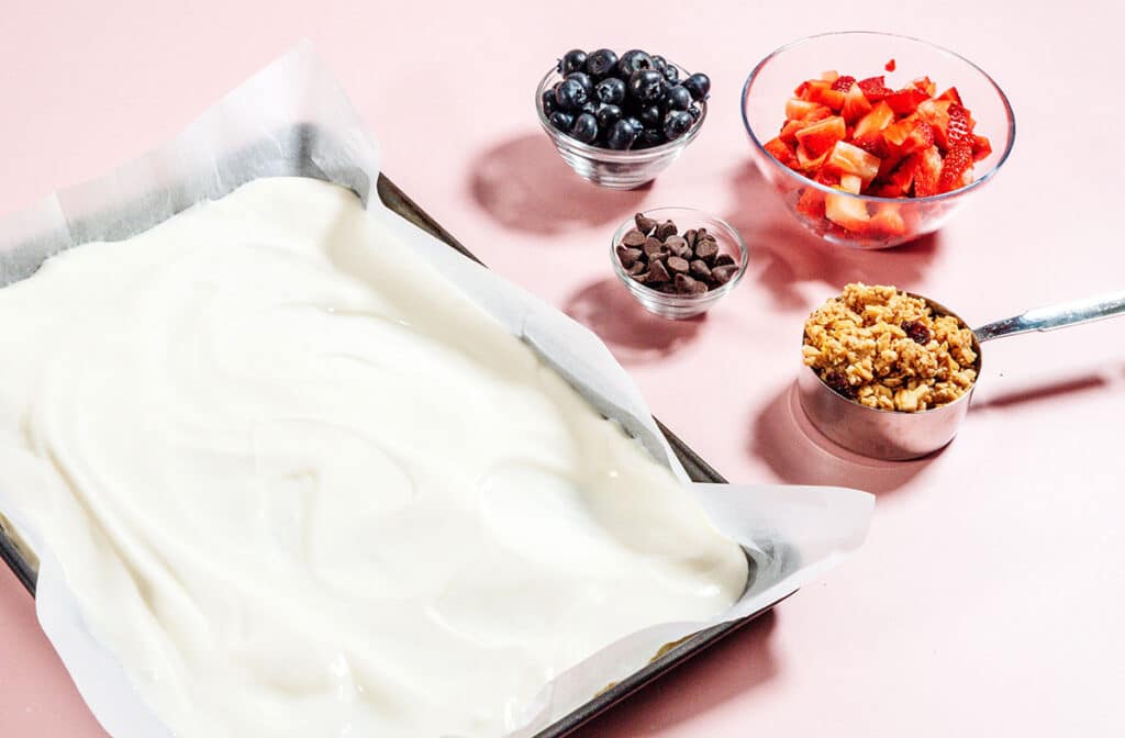 Yogurt on a baking sheet next to berries and granola.