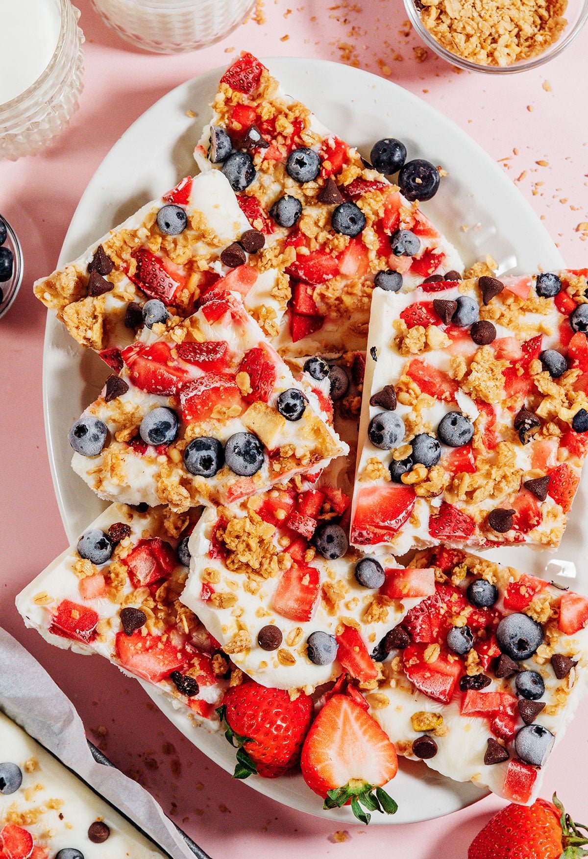 Frozen yogurt breakfast bark with berries and granola on a pink background.