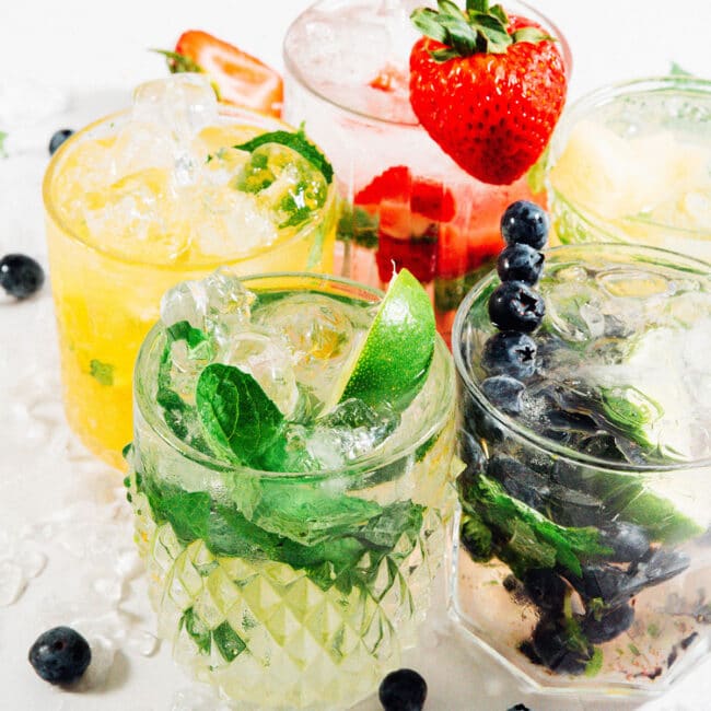 Many colors of fruity mojitos on a white table.