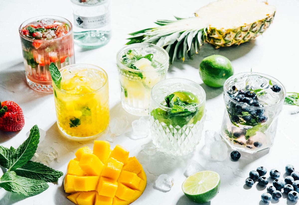 Many colors of fruity mojitos on a white table.
