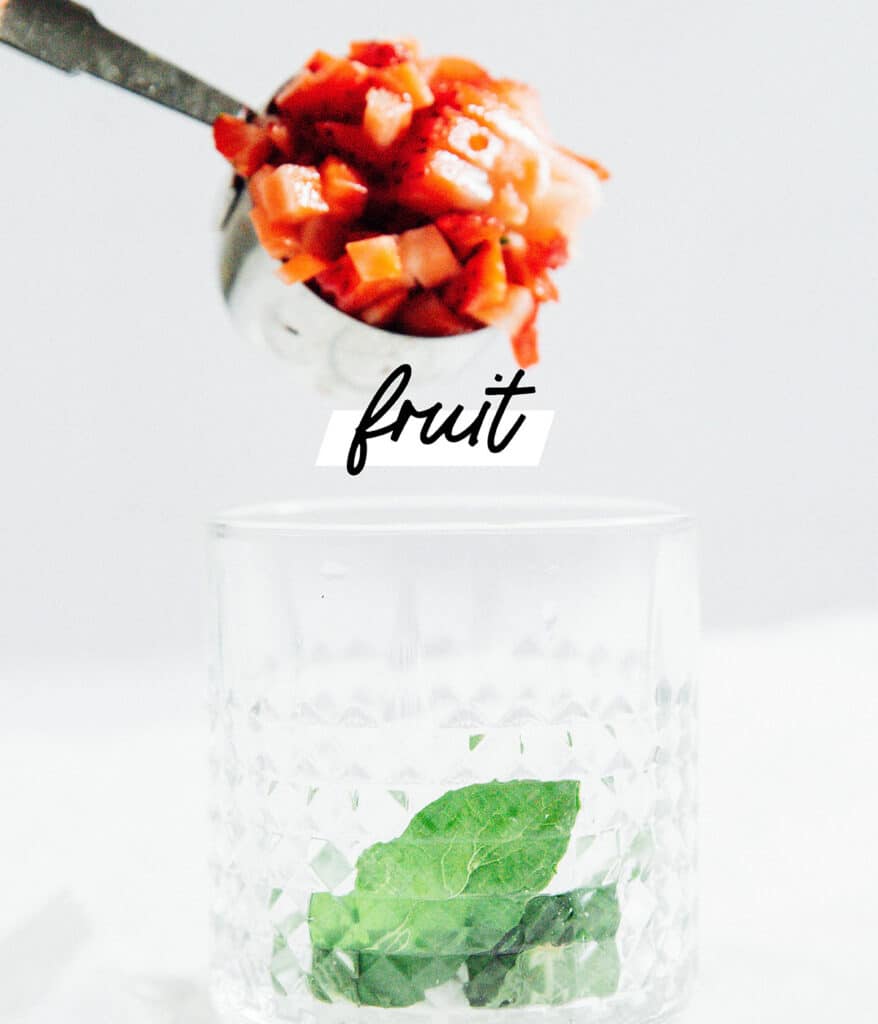 Adding fruit to a glass to make strawberry mojitos.