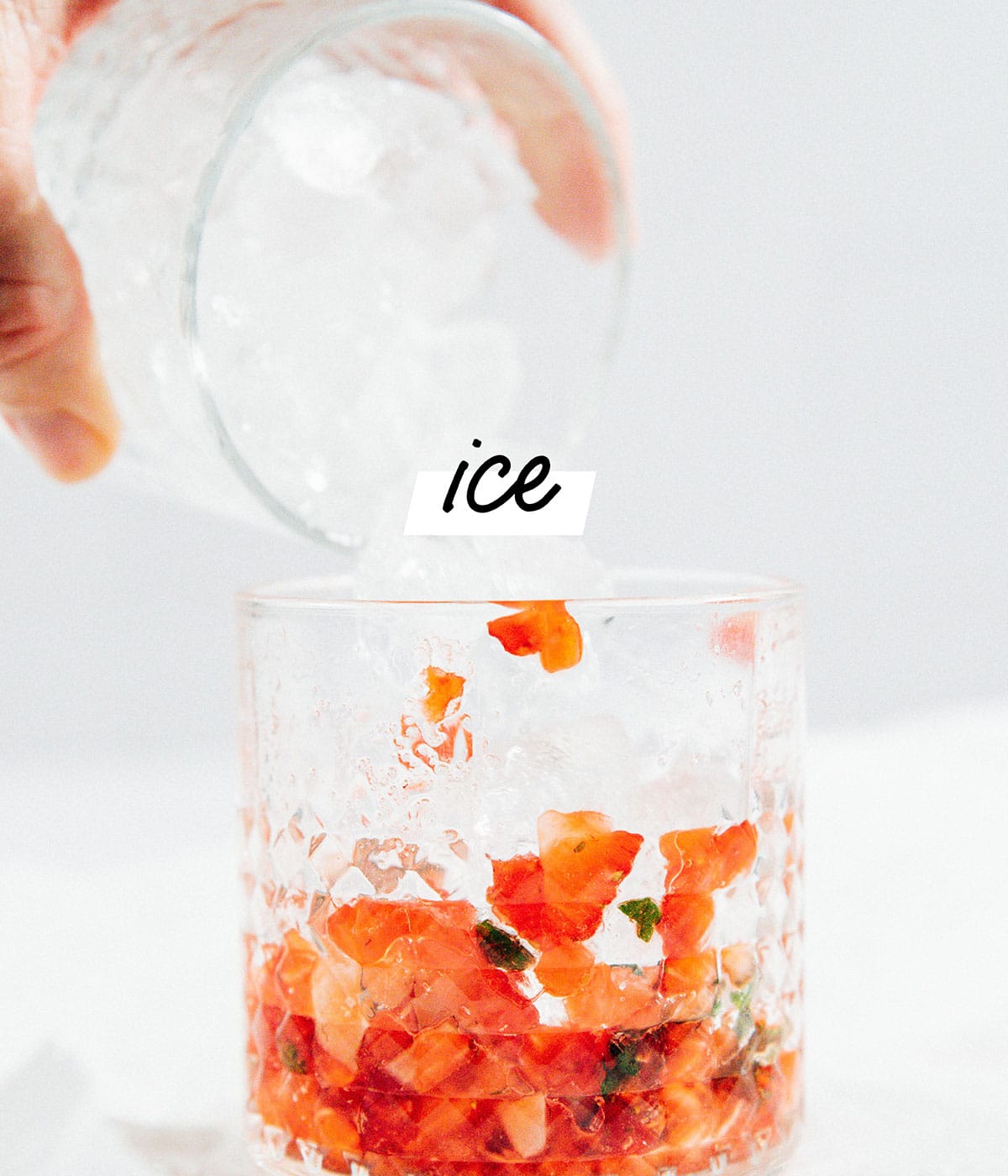 Adding ice to a glass to make strawberry mojitos.