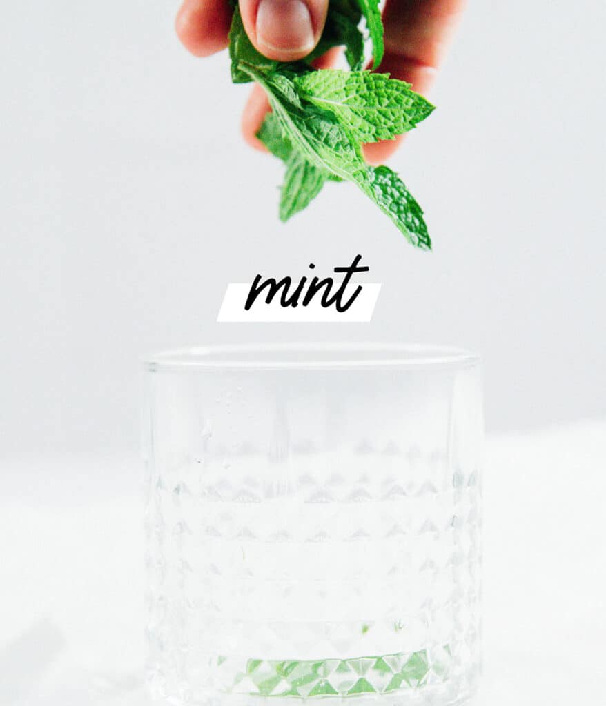 Adding mint to a glass to make strawberry mojitos.