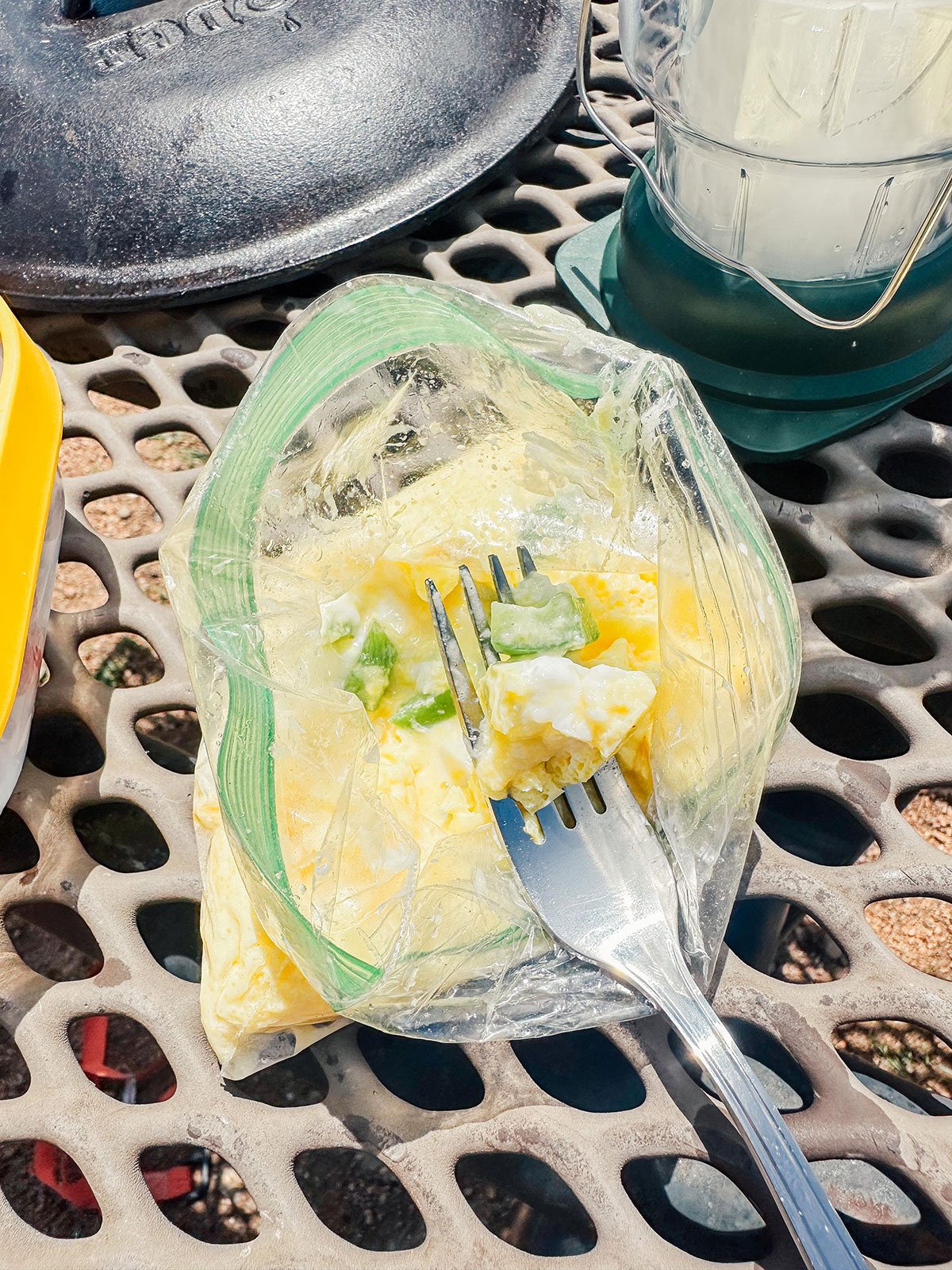 Scrambled eggs on a fork by a picnic table.