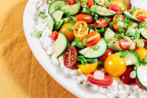 A refreshing cottage cheese salad featuring sliced cucumbers, cherry tomatoes, and chopped green onions, all seasoned with black pepper.