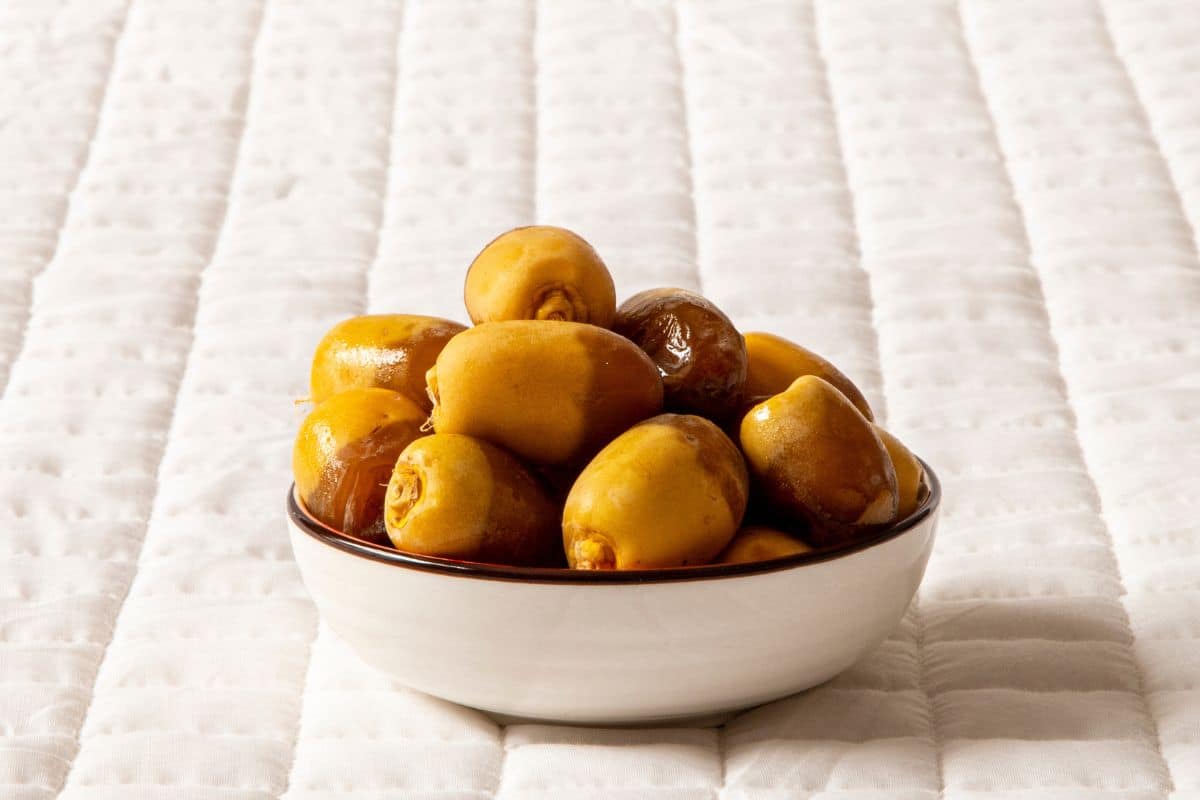 A bowl of maktoom dates on a white quilted background.
