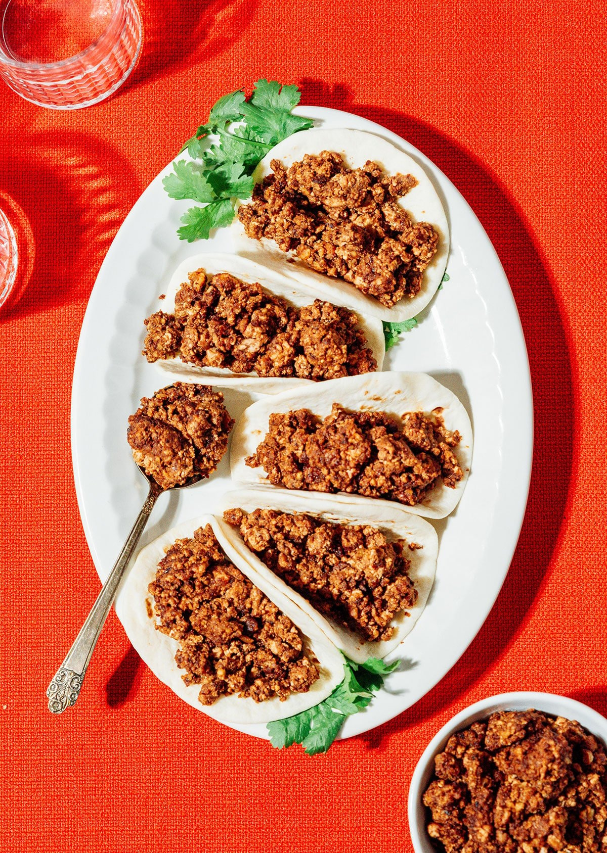 Vegan chorizo in tortillas on a platter with a red table cloth.
