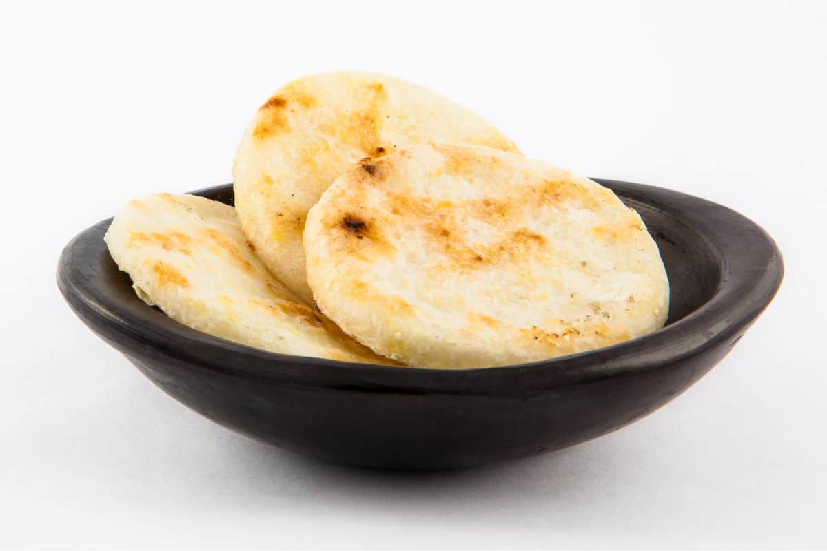 Arepa bread on a white background and in a bowl.