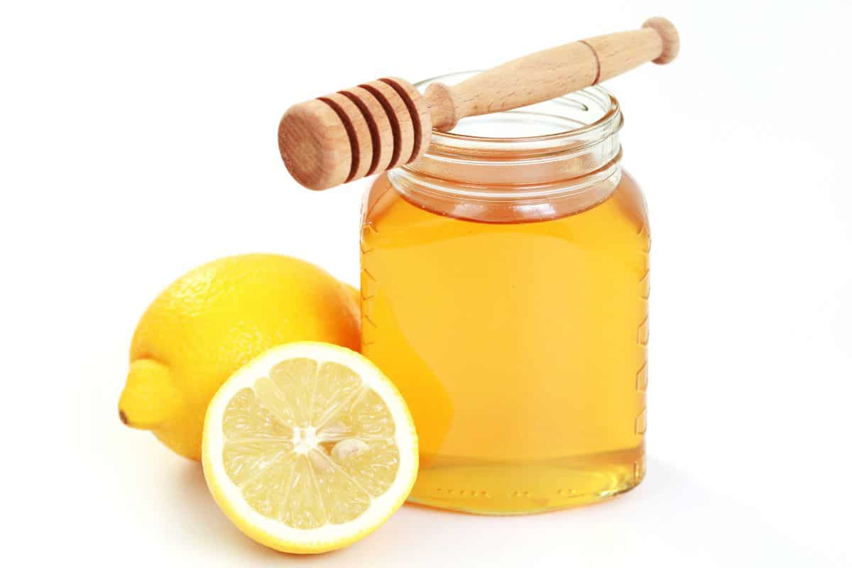 Citrus honey in a jar next to a lemon on an isolated white background.