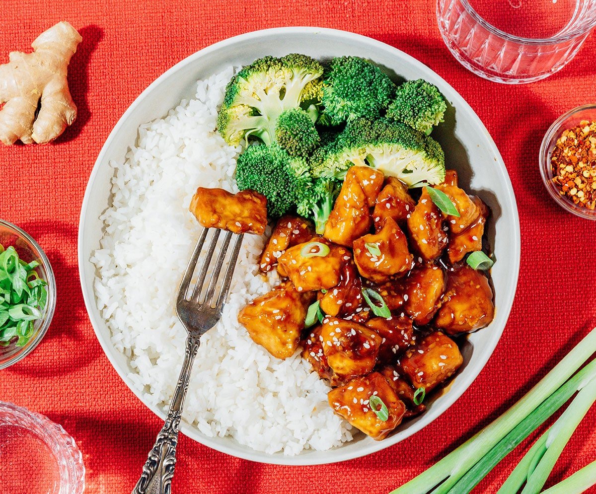 General tso's tofu in a bowl with rice and broccoli.